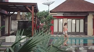 Girl in bikini walk along the open pool next to the summer house aerial footage