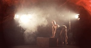 Female contortionist in dramatic smoky scene does chest stand on box