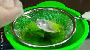 Cook stirring mixture in sieve with spoon in kitchen. Professional chef demonstrates appropriate way to cook sauce employing funnel