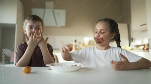 Child children eat sweet chocolate at table. Dirty face child mouth biting cocoa chocolate with teeth. Sweet breakfast of children at the table in kitchen. Happy kids with messy face eating chocolate