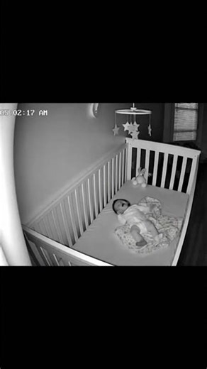 05:02AM—B&W Infrared Feed—A figure’s shadow stretches across the wall toward the crib.The baby cries