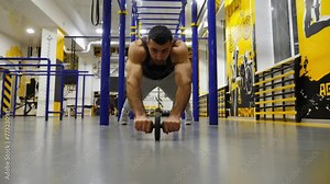 Strong sporty man doing exercises with ab roller at modern gym. Muscular athlete hard training with gymnastic wheel at fitness centre. Young sportsman working out at sport club. Healthy lifestyle