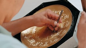 Master engraves patterns on a metal plate. Close-up, handmade, tinsmith, working with hammer during hand stamping or engraving decoration pattern on metal tray. Copper master, hands detail of