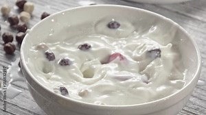 Ripe red strawberry fruit and corn balls fall into a white bowl with milk with a splash. Close-up, slow motion. The milk splash falls out of the bowl on the gray table. Full HD video, 240fps,1080p.