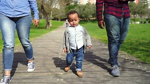 African American little boy walking with mom and dad in park. Front view of mother, father and son pacing on wooden footpath. Low camera position. Family and weekend concept