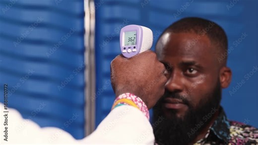 Closeup of African male doctor's hand using a non-contact thermometer to check a male patient's temperature during a consultation in a hospital