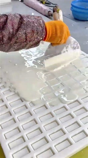 filling white liquid material into a rectangular grid mold using a metal spatula for even coverage