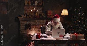 Bearded Santa Claus using laptop, outside view through window, typing on keyboard, buying New Year presents for children online. Grey-haired Saint Nicholas working at night on Christmas Eve.