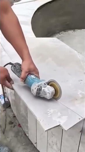 cutting a light grey ceramic tile using an electric grinder on a construction site