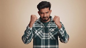 Aggressive angry young indian man trying to fight at camera, shaking fist, boxing with expression, punishment, quarrel. Displeased handsome bearded hindu guy isolated alone on beige studio background