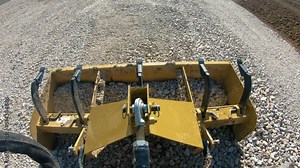 Box scrapper dropping to level a new graveled driveway and gravel collects in box; concepts of blue collar work, hydraulics, new construction and country life