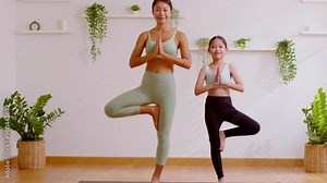 Healthy couple mom and little girl doing yoga one leg stand on yoga mat at home.Mother and female daughter practice yoga breathing exercise and meditate together calm and comfort.Happy Family Activity