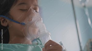 Asian girl having an oxygen mask and breathing through a nebulizer at the hospital.