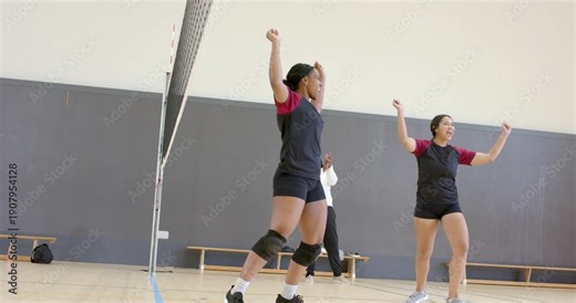 Coach clapping sparking female volleyball players raising arms and forming huddle near net on court