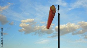 Orange windsock being moved by the wind with a blue sky and some clouds as a background. Close up, Time-lapse shot during the afternoon.