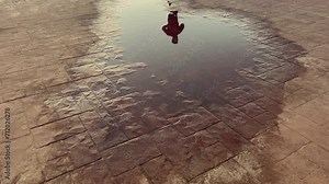 Slow motion shot of a jogger running on a walkway as reflected by a puddle of water