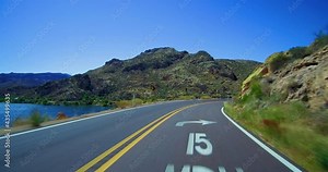 Following a vehicle in the distance on scenic curvy mountain Apache Trail road with partial views of Canyon Lake Arizona crossing over one lane bridge.
