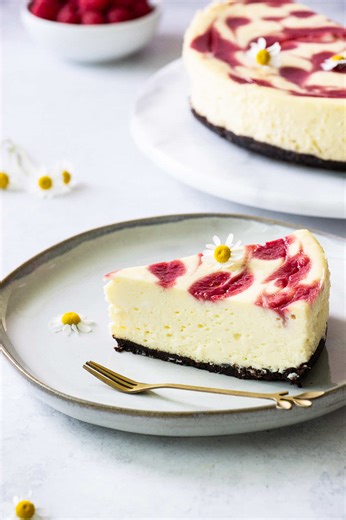 White Chocolate Raspberry Swirl Cheesecake… Imagine a creamy, velvety white chocolate cheesecake base perfectly balanced with the bright, tangy sweetness of fresh raspberries swirled throughout. Each bite is a beautiful harmony of rich and refreshing flavors—making this dessert an irresistible treat for any occasion. INGREDIENTS For the Base 1½ cups finely ground graham crackers ⅓ cup extra dark cocoa powder ¼ cup melted butter For the Filling 4 (8 oz) blocks cream cheese, room temperature 2 bar