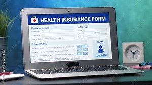 Laptop computer with a health insurance application form on its display. Camera turning slowly around the desk.