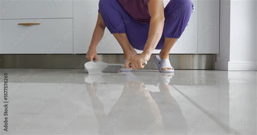 Woman cleaning tiled floor at home with dustpan and brush