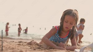 Little girl playing on beach on summer vacation Little girl builds sand castle with crowd tourist at ocean background. Enjoy the summer vacation. Have fun on the beach