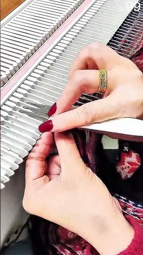 Knitting machine aligns yarn loops; tool guides threads across white needles precisely