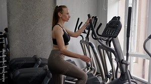 A young slender woman in excellent athletic shape enters the gym and customize the operation of the leg exercise machine. Hand movement and pedaling. The concept of sports lifestyle and healthy