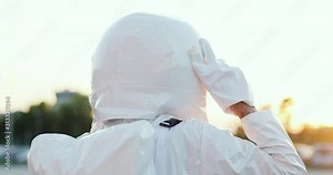 Close up of the rear of Caucasian young man astronaut taking on head armor and walking to the launching place. Journey in the space. Back view. Outside.
