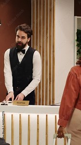 Vertical Video Helpful front desk receptionists answering customer inquiries about hotel facilities during guests check in process. Cheerful smiling concierge coworkers assisting visitors with room