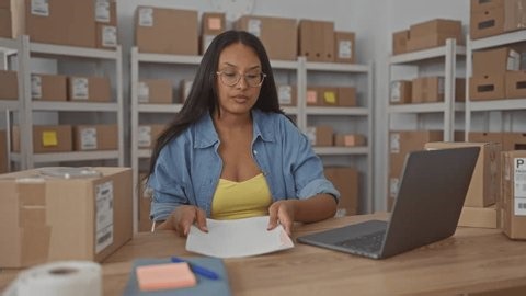 clip-3988495915-woman-typing-on-laptop-handling-shipping-papers