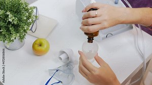 A woman pours expectorant medicine from a bottle into a portable inhaler or nebulizer.