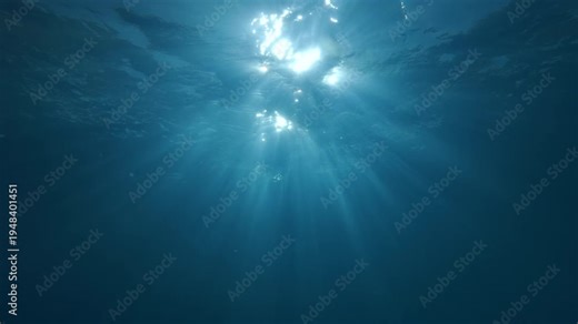 View on sunlight from depth sea, slow motion. Dancing sunbeams play below surface of water. Sunshine filters down through blue water. Undersea dance sun rays in Ocean. Sunburst shines underwater