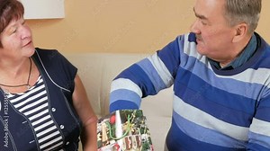 Happy senior man gives a woman's gift in package. He pulls out a pearl necklace and trying on her neck. Husband and wife in a beautiful house in Christmas