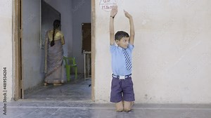 Kid peeking inside classroom after been sent from out as punishment while standing on kee with hands up - concept of childhood mischief and education.