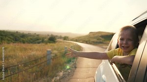 Teen looking out car window and waving his hand. Family travel by car. Hand to wind of freedom. Cheerful boy smiles. Happy family concept. Boy in car window. Wind of freedom at sunset.Vacation concept