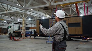 Construction worker supervising prefabricated house loading in factory