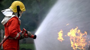 Brave firefighter in fire protection suit on safety rescue duty spray water from fire hose extinguishing crackle fire flames inside danger burning premises. Fireman fighting a fire in training area