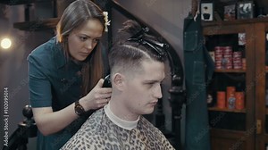 Woman barber cuts the hair of the client with clipper at barbershop