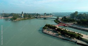 Wide aerial shot of Holy city Haridwar showing the big statue of Hindu God Lord Shiva,blue shining flowing water of Ganges river, bridge over holy Ganges River and traffic passing by the bridge.