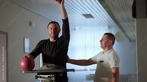 Male patient performs rehabilitation exercises with red balls, assisted by a physical therapist in a medical facility. Concept of physical therapy, shoulder recovery, and guided rehabilitation. Stock Video