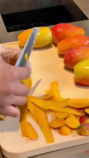 slicing ripe yellow mangoes on cutting board using sharp kitchen knife for fresh fruit preparation