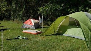 Two men finishing setting up small tents by putting rain cover while larger tent is already prepared for sleepover.