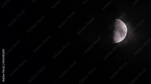 First quarter moon or waxing gibbous with amazing craters moving among mysterious clouds at night. Telephoto view, real midnight footage with black background. Creepy halloween sky, astrology concept.
