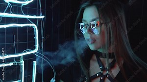 Confident and elegant woman with glasses in purple blue light smokes an electronic cigarette at a party near neon lights. Cute female close-up