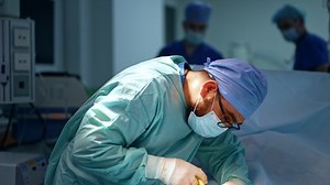 Careful focused anesthesiologist giving injection to the patient. Doctor holding a syringe bent over the person on surgical table.