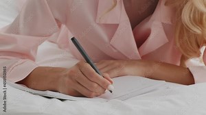 Unrecognizable woman writing in notepad while lying on bed at home