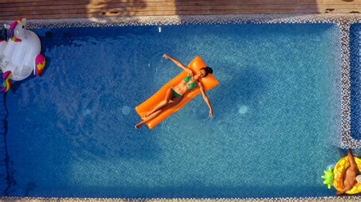 Aerial view of a young woman wearing a colorful bikini enjoying the swimming pool over an orange floaty - Free Stock Video
