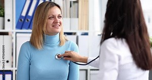 Doctor therapist listening with stethoscope to woman patient in clinic 4k movie slow motion. Heart and lung auscultation concept