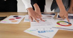 Closeup of hand pointing and explaining the information on the paper with team in the meeting room. Businessman and businesswoman meeting on sales pitch.