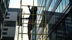 Girl model with a beautiful figure in the helmet. She poses in a yellow iron cage against the backdrop of modern buildings. Center of Moscow street style.